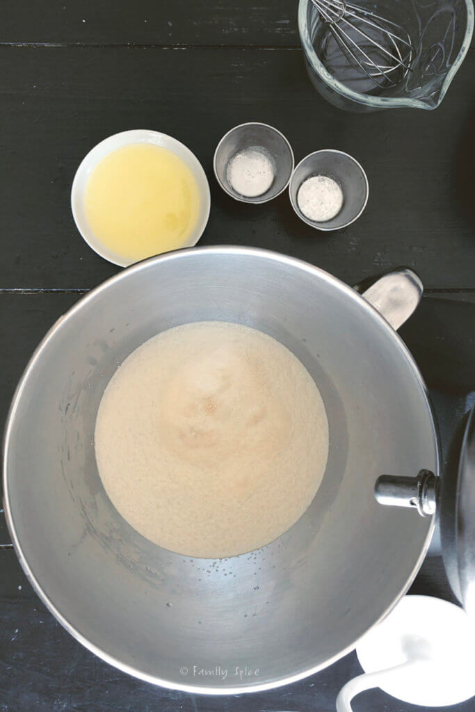 Yeast foaming in a stainless bowl with warm water with other ingredients around it