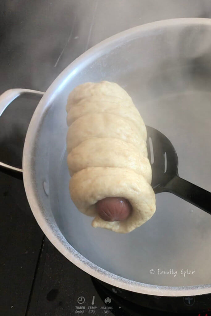 Removing a pretzel dough wrapped hot dog out of hot water bath