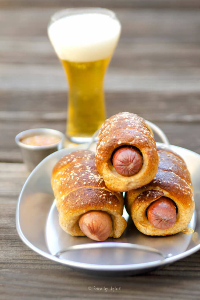 Closeup on whole wheat pretzel dogs on a metal tray with a glass of beer behind it