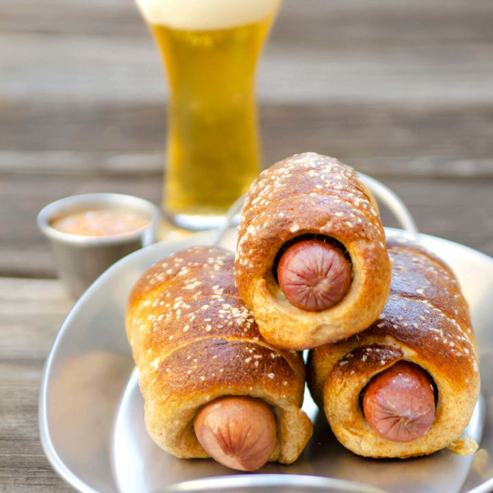 Closeup on whole wheat pretzel dogs on a metal tray with a glass of beer behind it