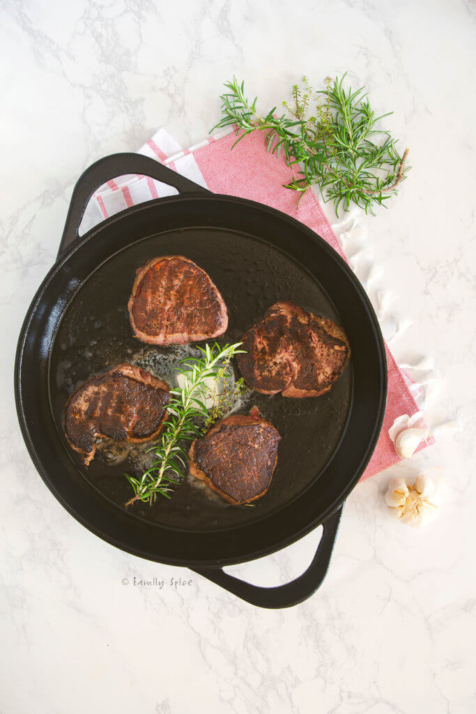 Seared filet mignons in a cast iron pan with melted butter and herbs in it