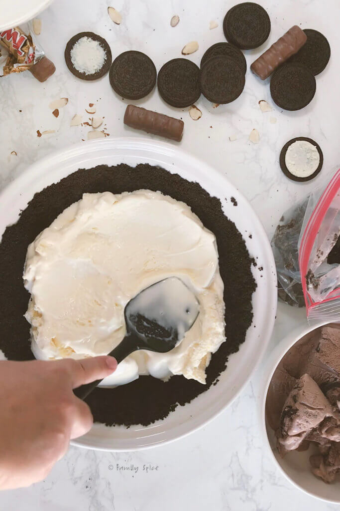 Spreading a layer of vanilla ice cream into an Oreo pie shell for a mud pie