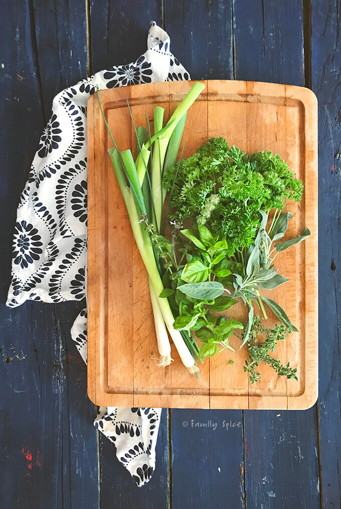 An assortment of fresh herbs on a wooden cutting board by FamilySpice.com