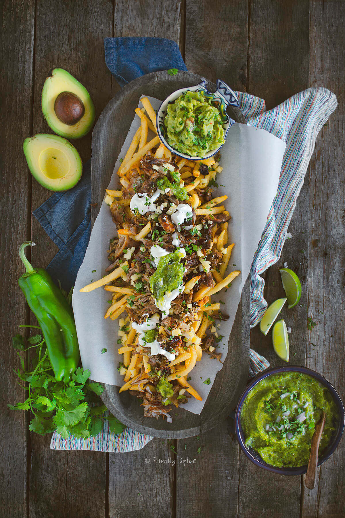 Top view of a platter of french fries topped with shredded pork chile verde, cheese, guacamole and sour cream