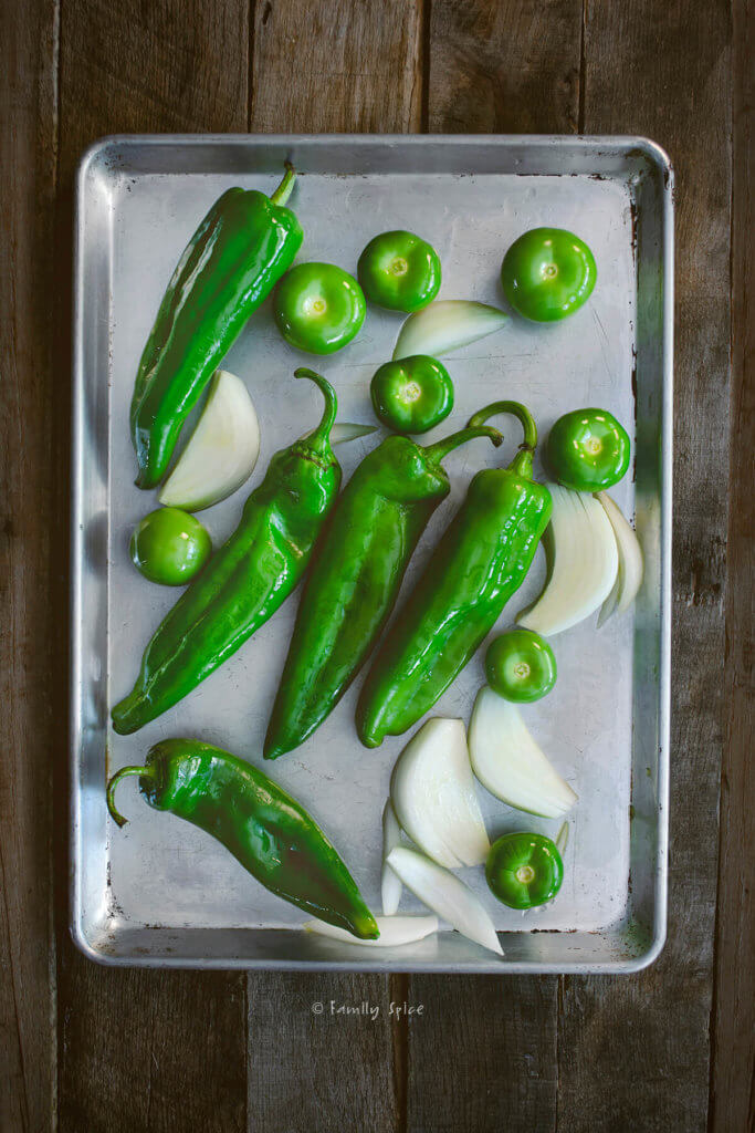 A baking sheet with green chiles, onions and tomatillos on it