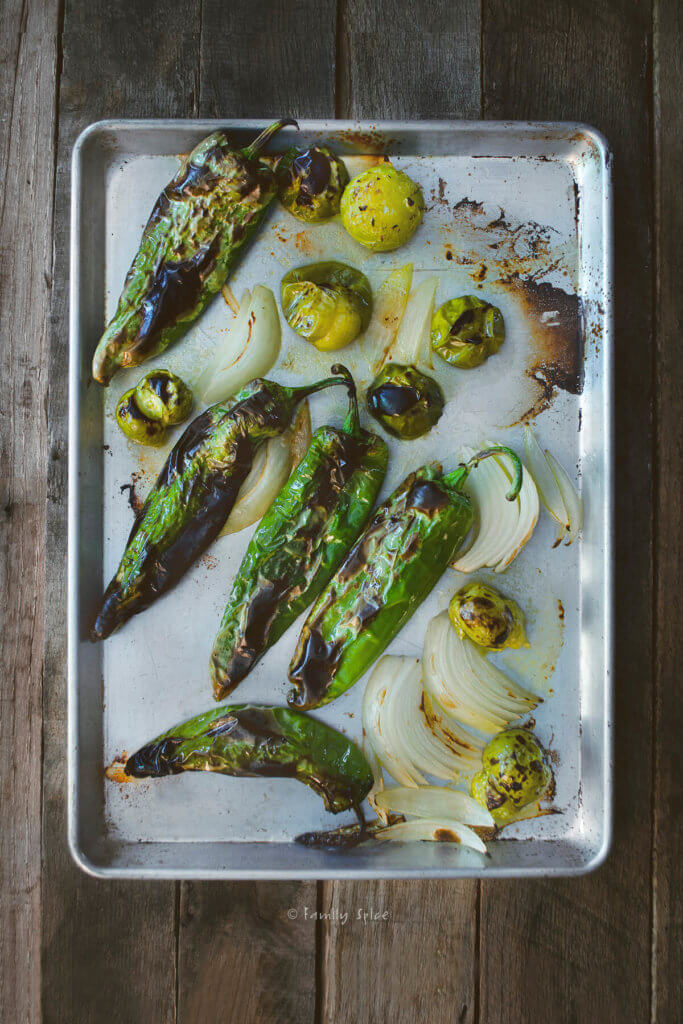 A baking sheet with freshly roasted green chiles, onions and tomatillos on it