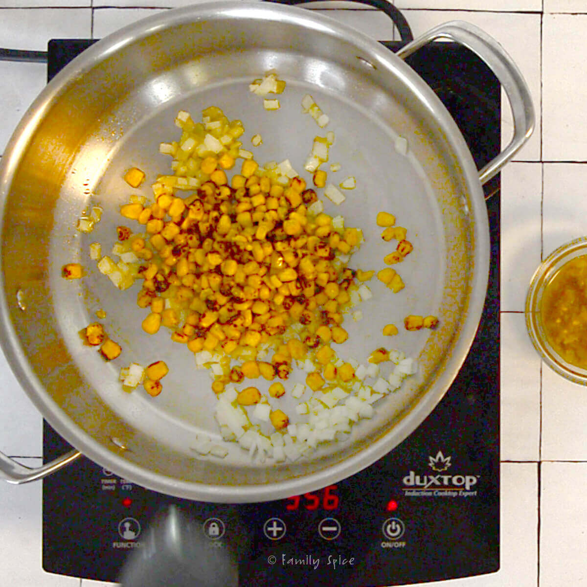A stainless pot with sautéed onions and corn in it