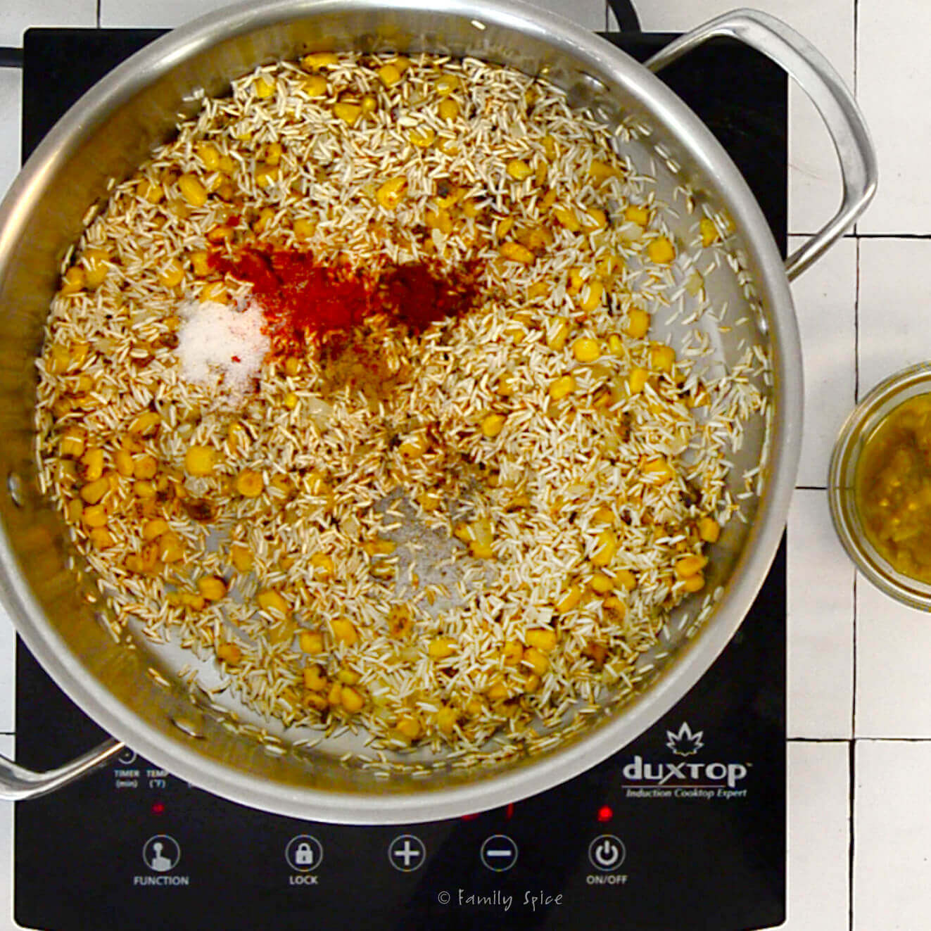 A stainless pot with sautéed onions, corn rice and spices in it