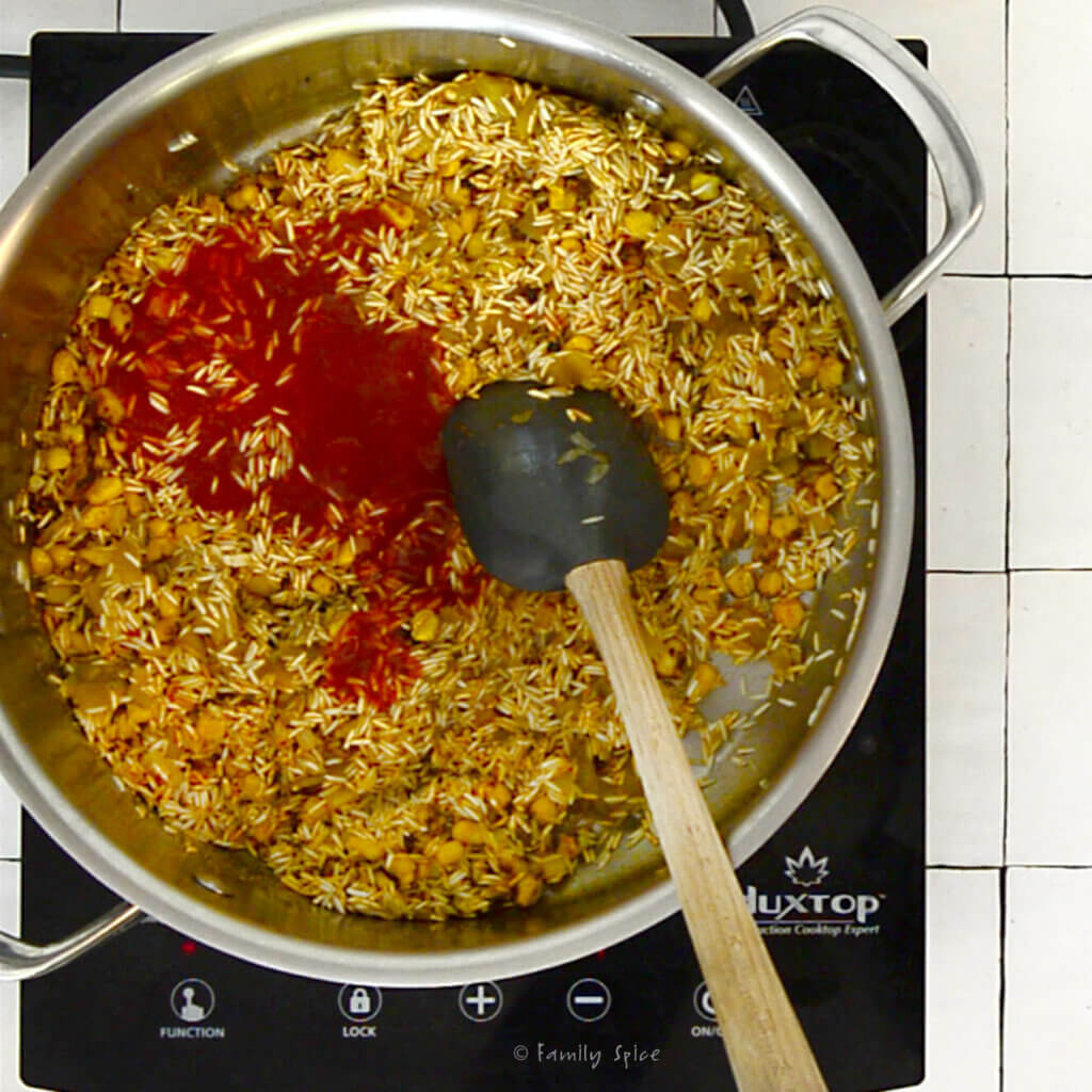 A stainless pot with tomato sauce added to toasted rice
