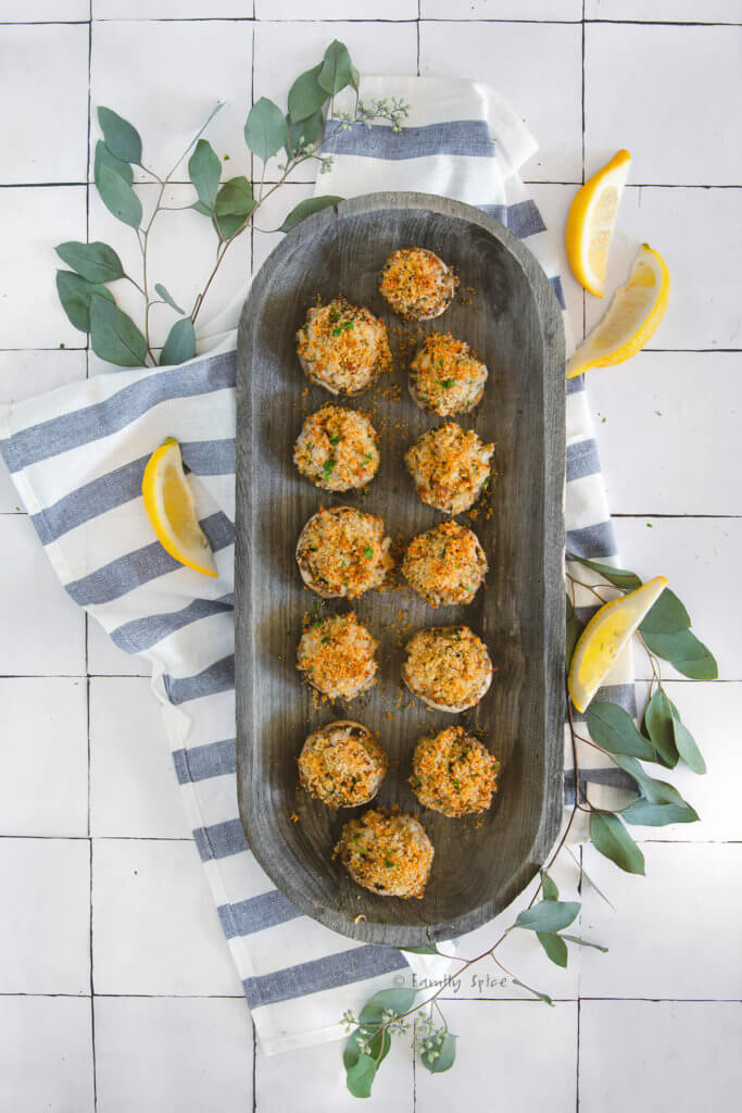 Overhead shot of a wooden platter filled with crab stuffed mushrooms and lemon slices