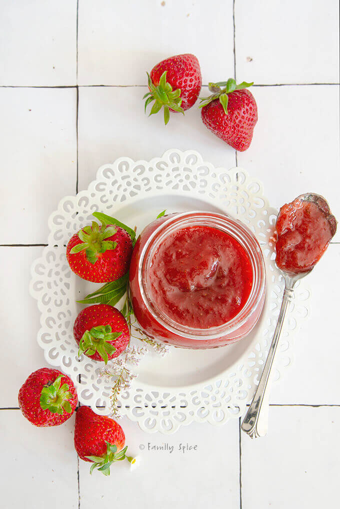 Overhead view of a bottle of strawberry rhubarb jam surrounded by fresh strawberries with a spoon of jam next to it
