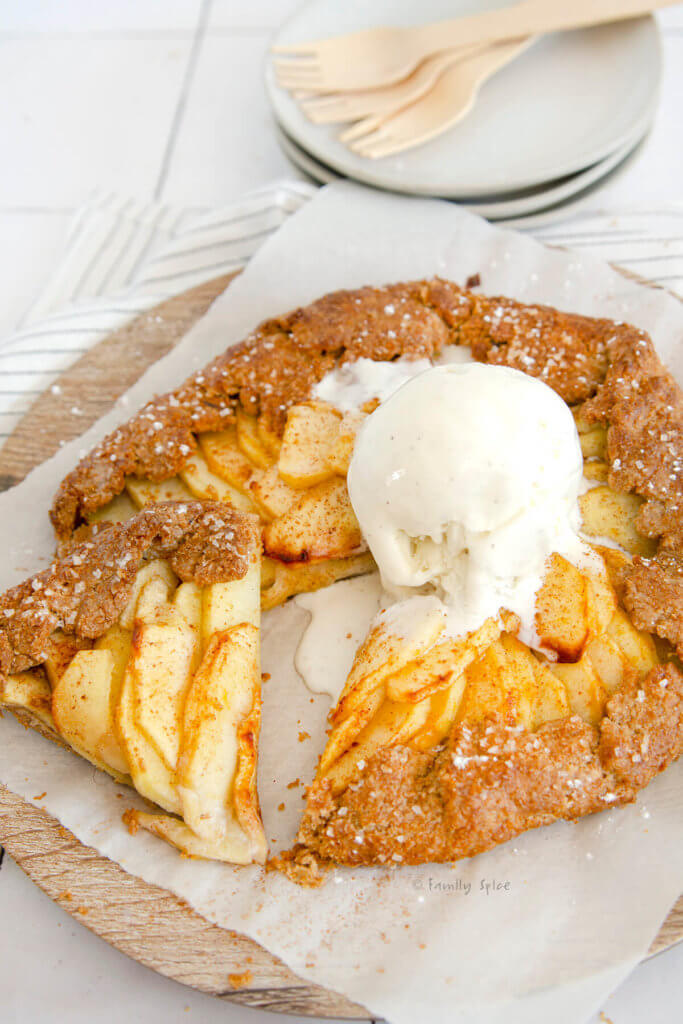 Closeup of a freshly baked whole wheat apple galette topped with vanilla ice cream with a small slice cut out