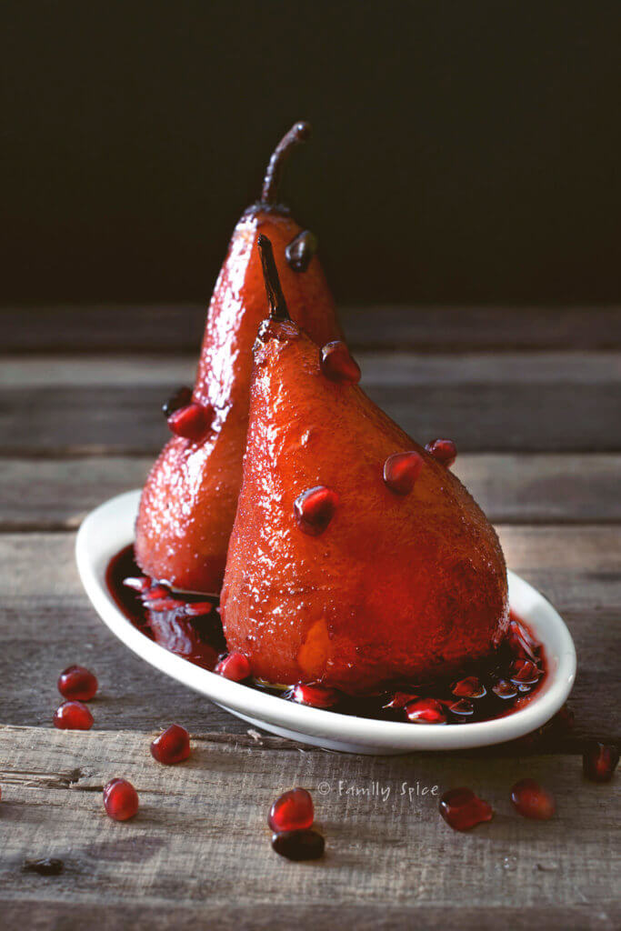 Ruby red poached pears garnished with pomegranate arils on a rustic background