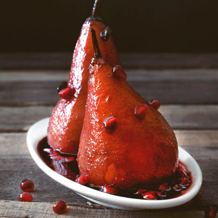 Ruby red poached pears garnished with pomegranate arils on a rustic background