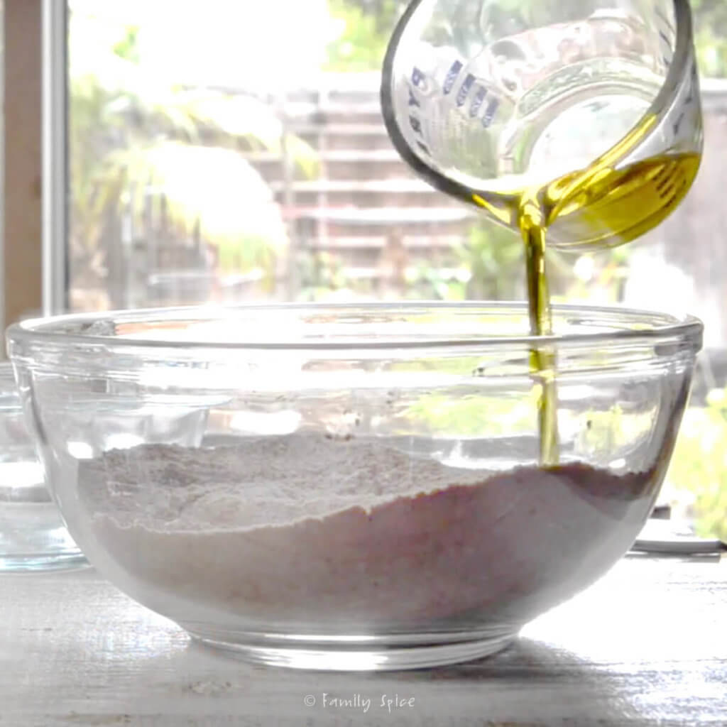 Adding olive oil into dry ingredients in a glass bowl to make chocolate pie dough