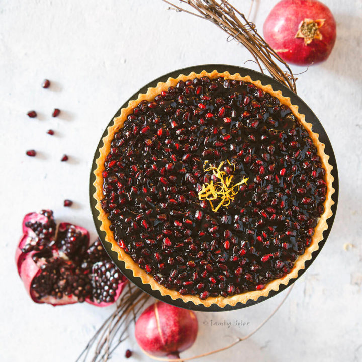 Overhead view of a pomegranate fruit tart garnished with lemon zest with pomegranates around it