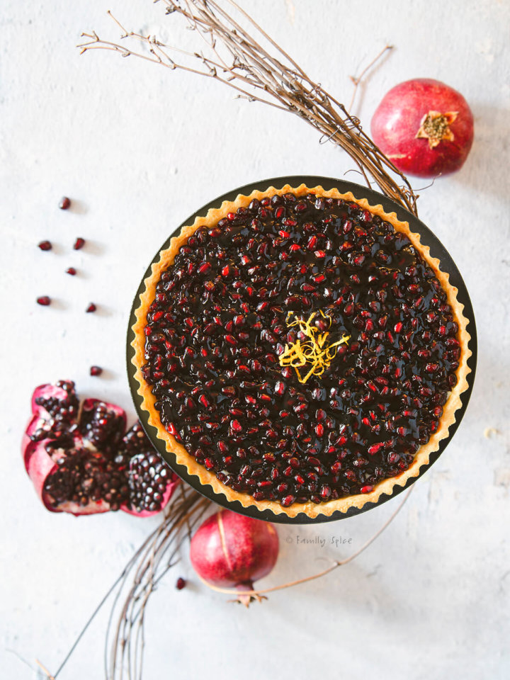 Overhead view of a pomegranate fruit tart garnished with lemon zest with pomegranates around it