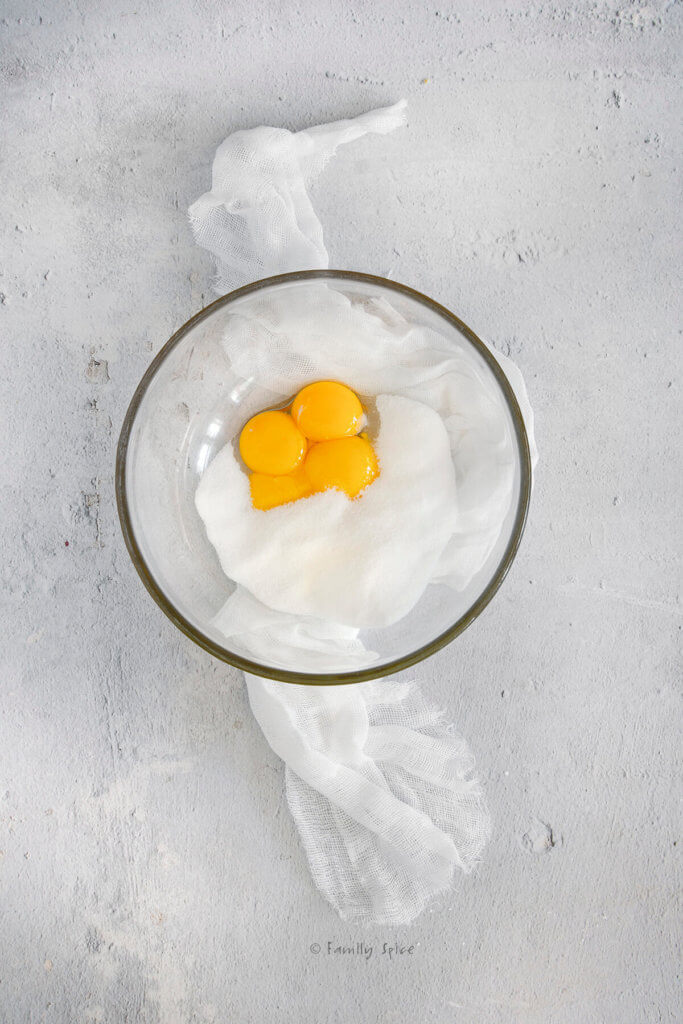 A glass mixing bowl with egg yolks and granulated sugar