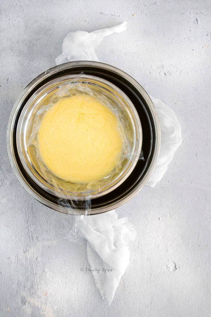 Pastry cream cooling off in a metal bowl covered in plastic wrap