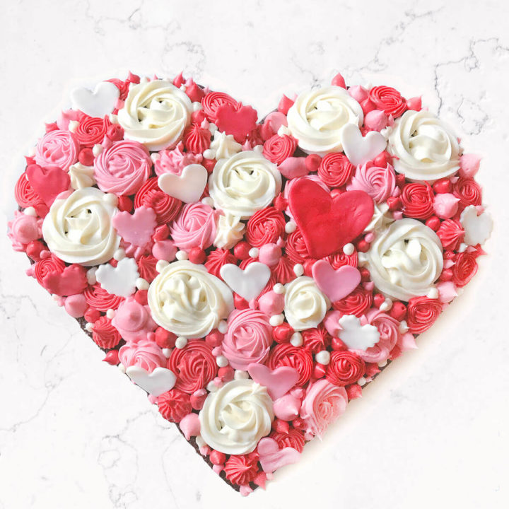 Chocolate heart cake decorated in various colored rosettes and studded with fondant hearts