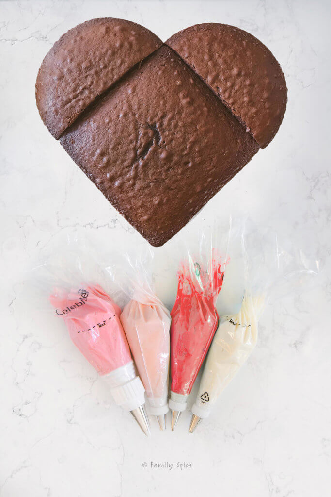 Chocolate heart cake with piping bags next to filled with frosting of different colors