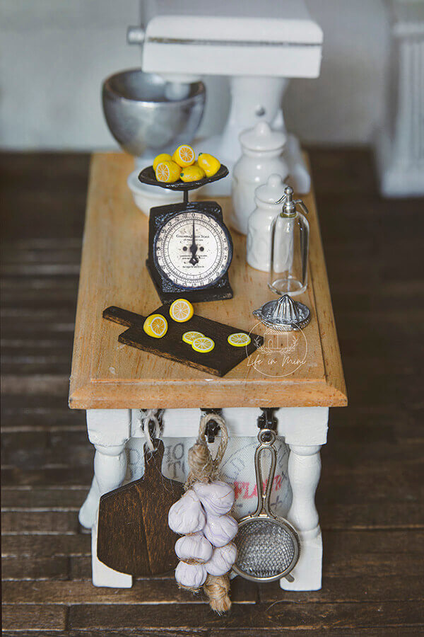 A dollhouse kitchen counter with miniature scale and lemons on a cutting board