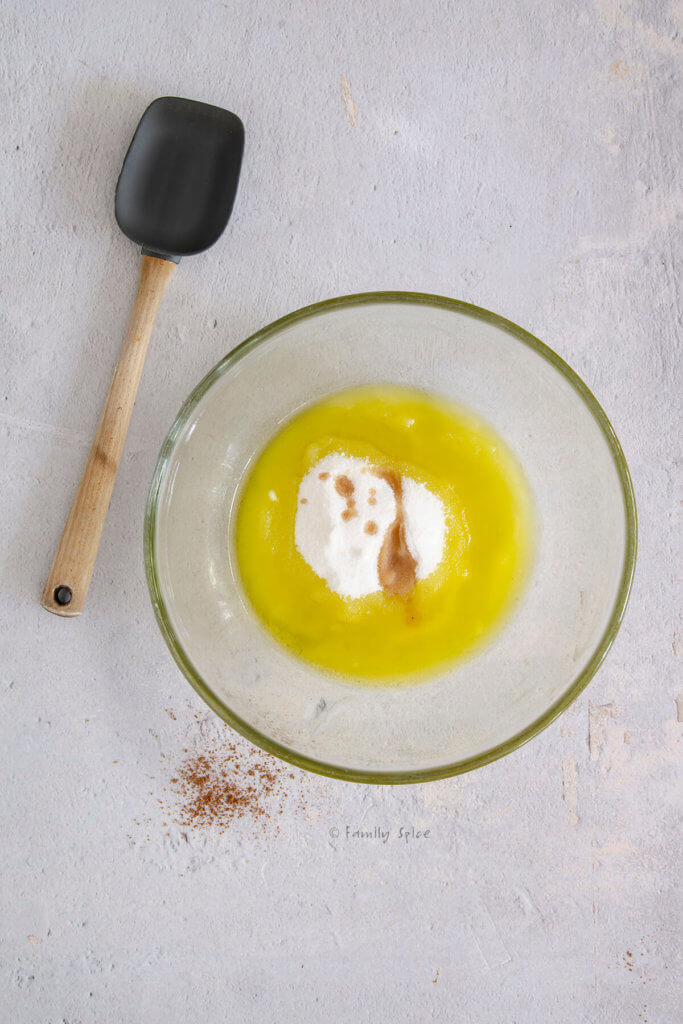 A large glass mixing bowl with sugar, vanilla extract and olive oil in it