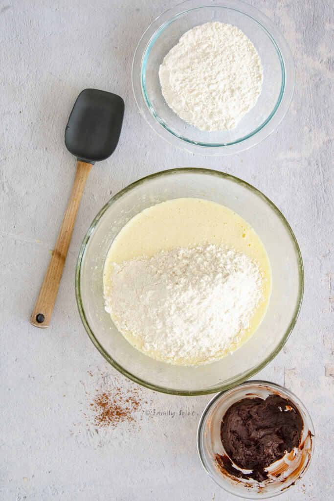 Adding flour to cake batter with a bowl of flour and cocoa paste next to it