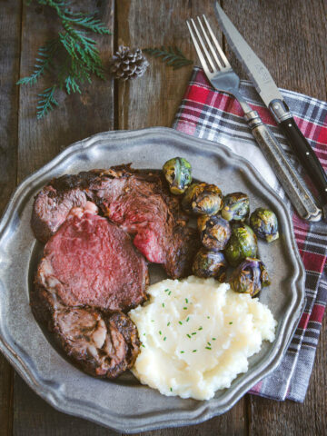 A plate of a slice of deep fried prime rib with mashed potatoes and Brussels sprouts