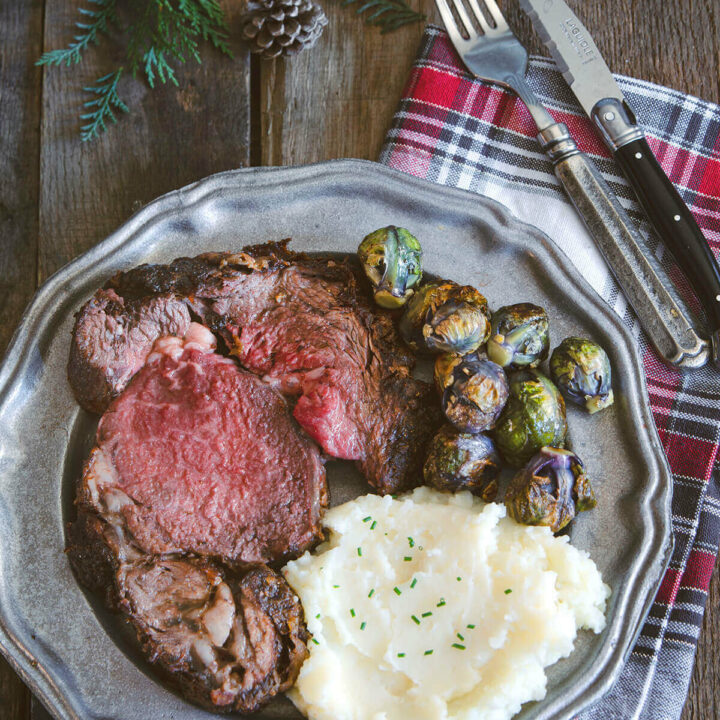 A plate of a slice of deep fried prime rib with mashed potatoes and Brussels sprouts