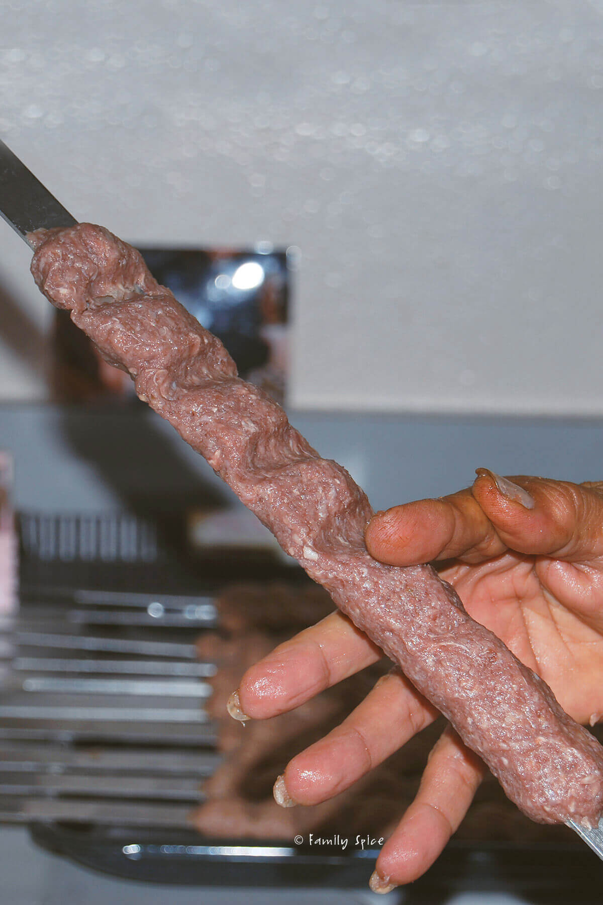 Using fingers to pinch koobideh kebab onto metal skewers