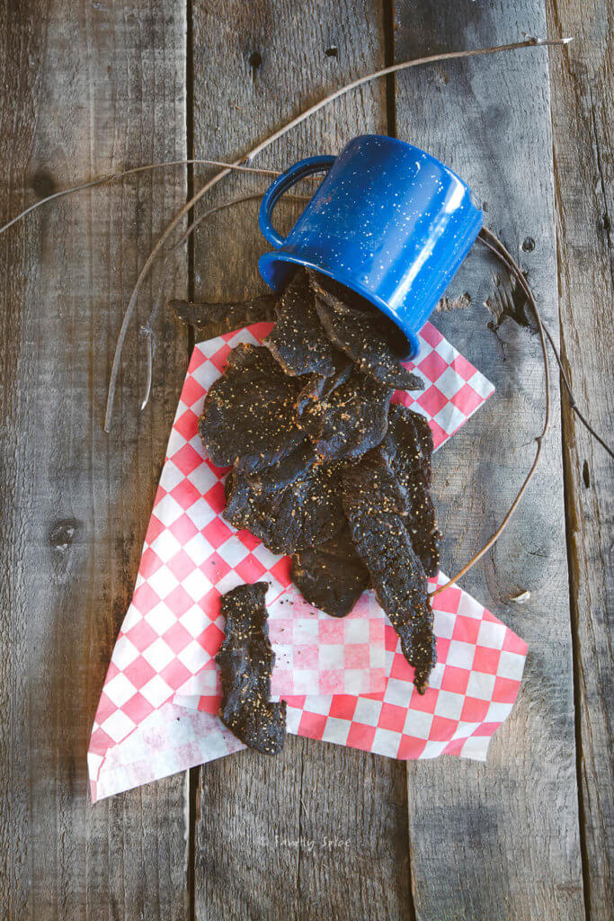 Overhead shot of oven beef jerky spilled out of a blue enamel mug