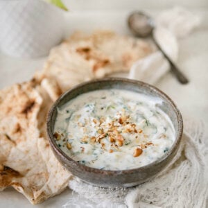 Side view of a bowl with spinach borani in it and lavash bread around it.
