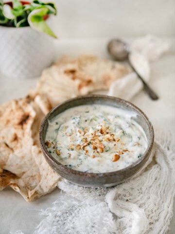 Side view of a bowl with spinach borani in it and lavash bread around it.