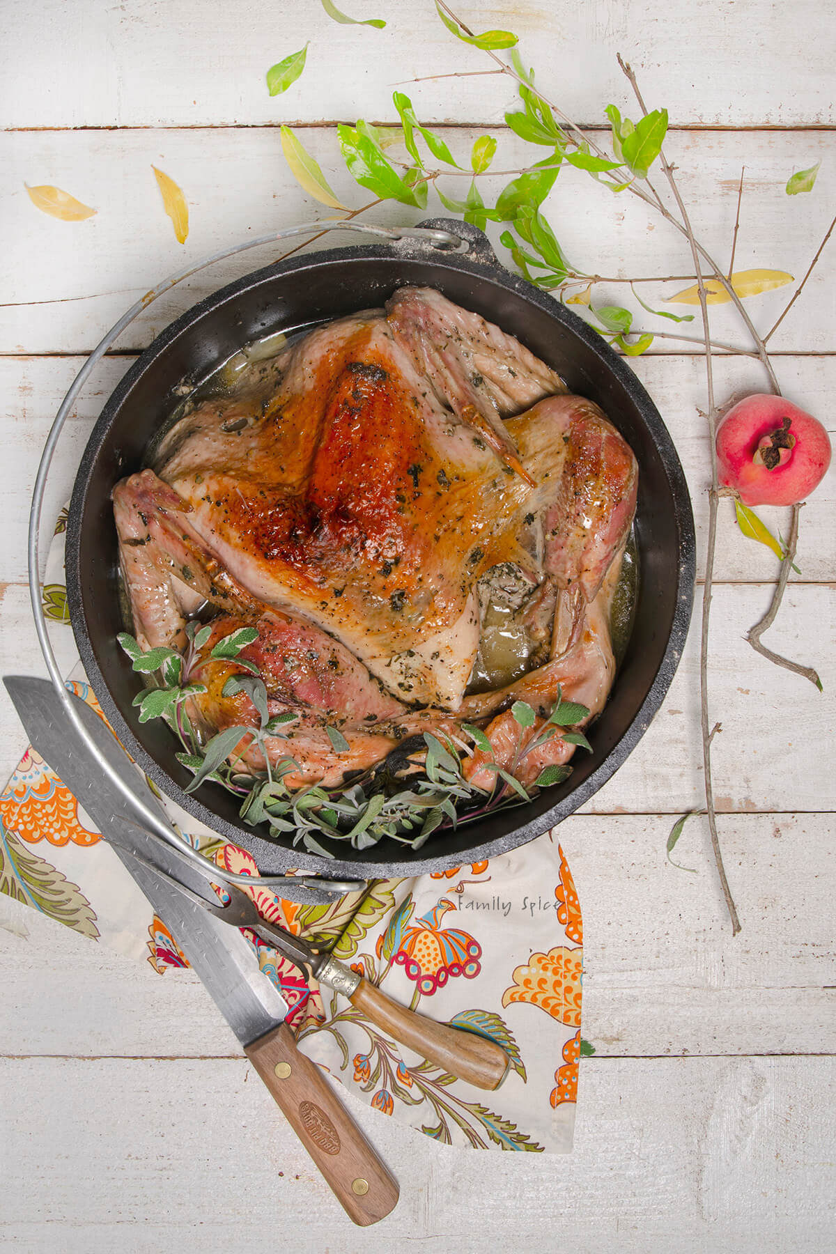 A roast turkey in a cast iron dutch oven garnished with fresh sage with carving knife and fork next to it