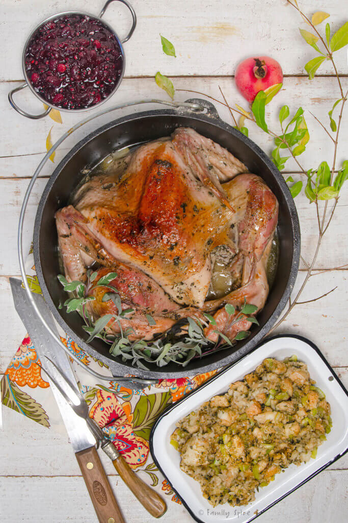 A roast turkey in a cast iron dutch oven with dressing and cranberry sauce next to it