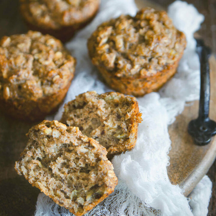 Closeup of one banana oatmeal muffin split in half with other muffins behind it