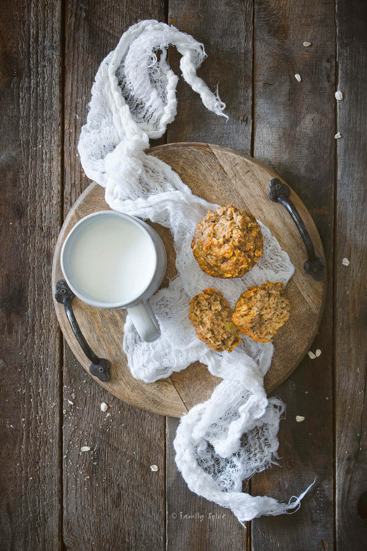 Overhead view of a small wooden tray with a mug of milk and a couple banana oatmeal muffins