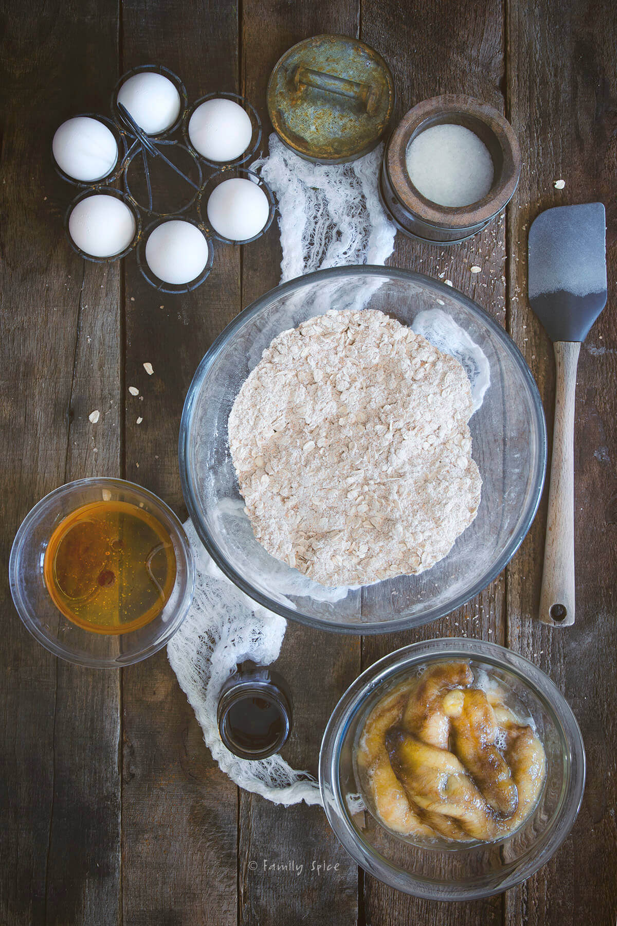 Flours in one bowl, a bowl with honey, another bowl with mashed bananas and eggs to make oatmeal muffins
