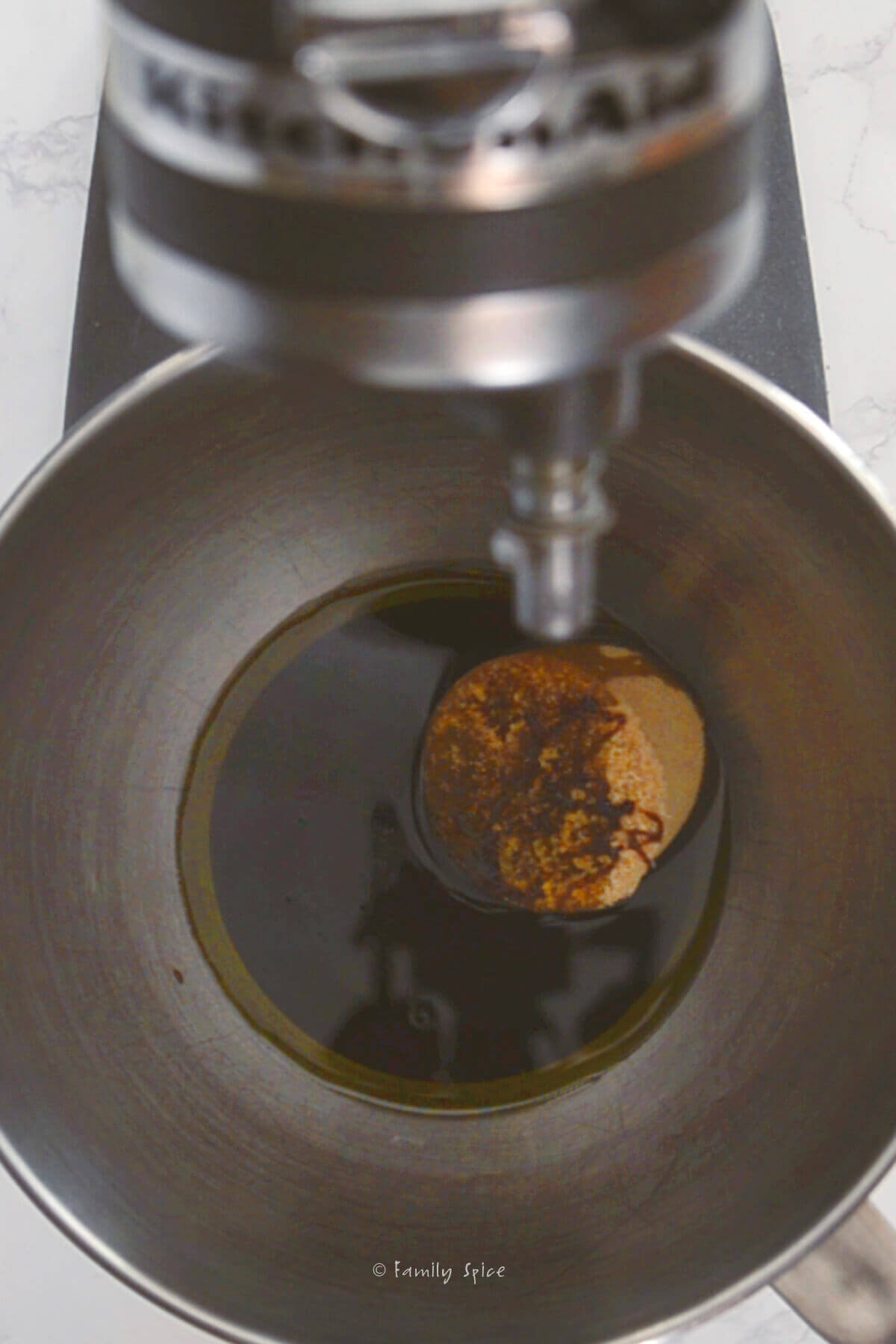 A stand mixer with olive oil, molasses and brown sugar in the bowl
