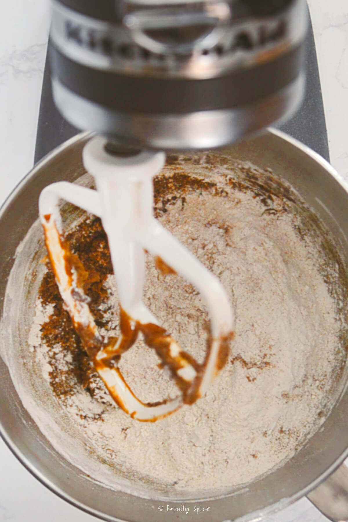 A stand mixer with flour mix added into the bowl holding the molasses mixture