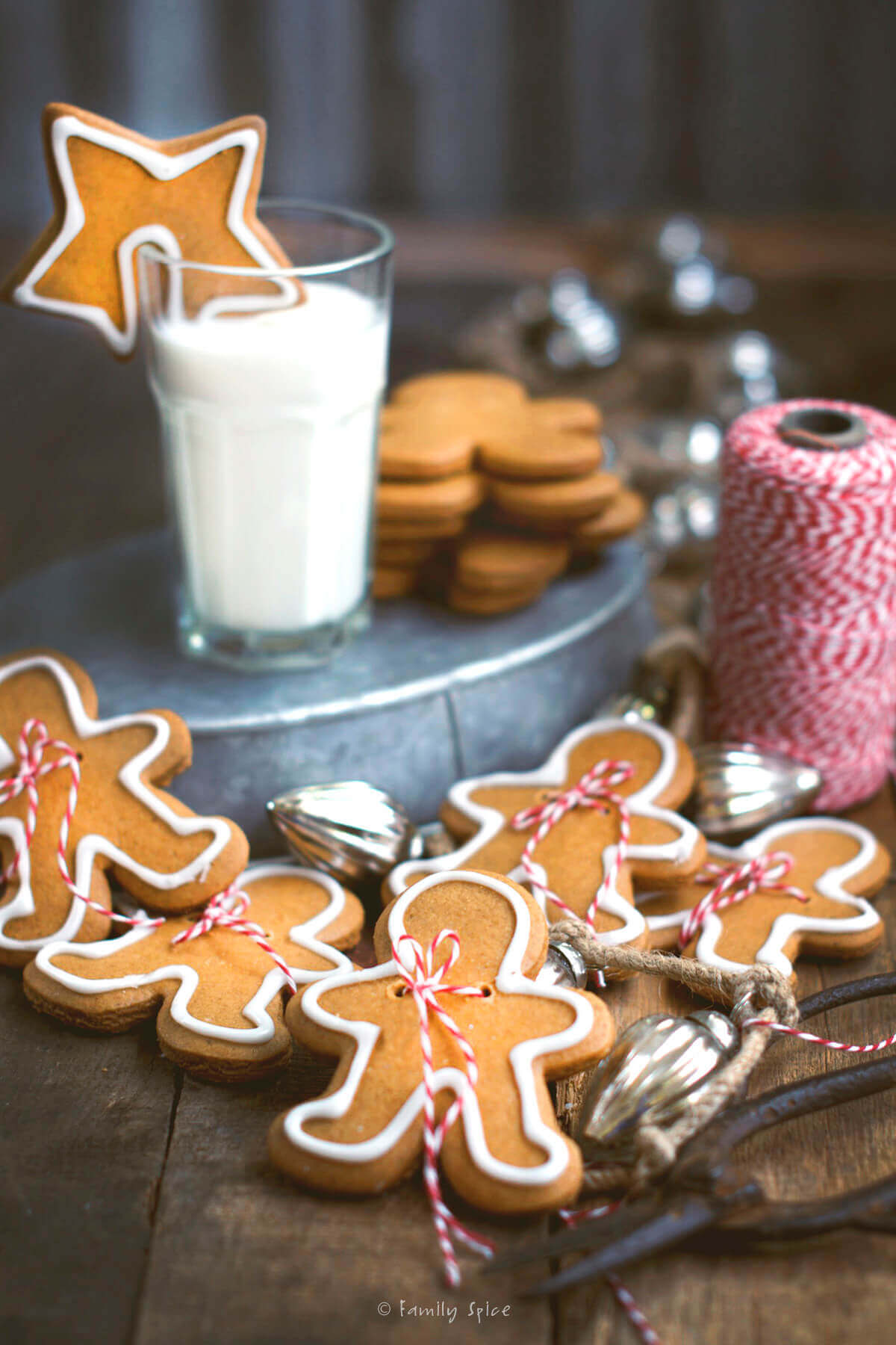 A star gingerbread cookie on a glass of milk in the background with gingerbread men around it