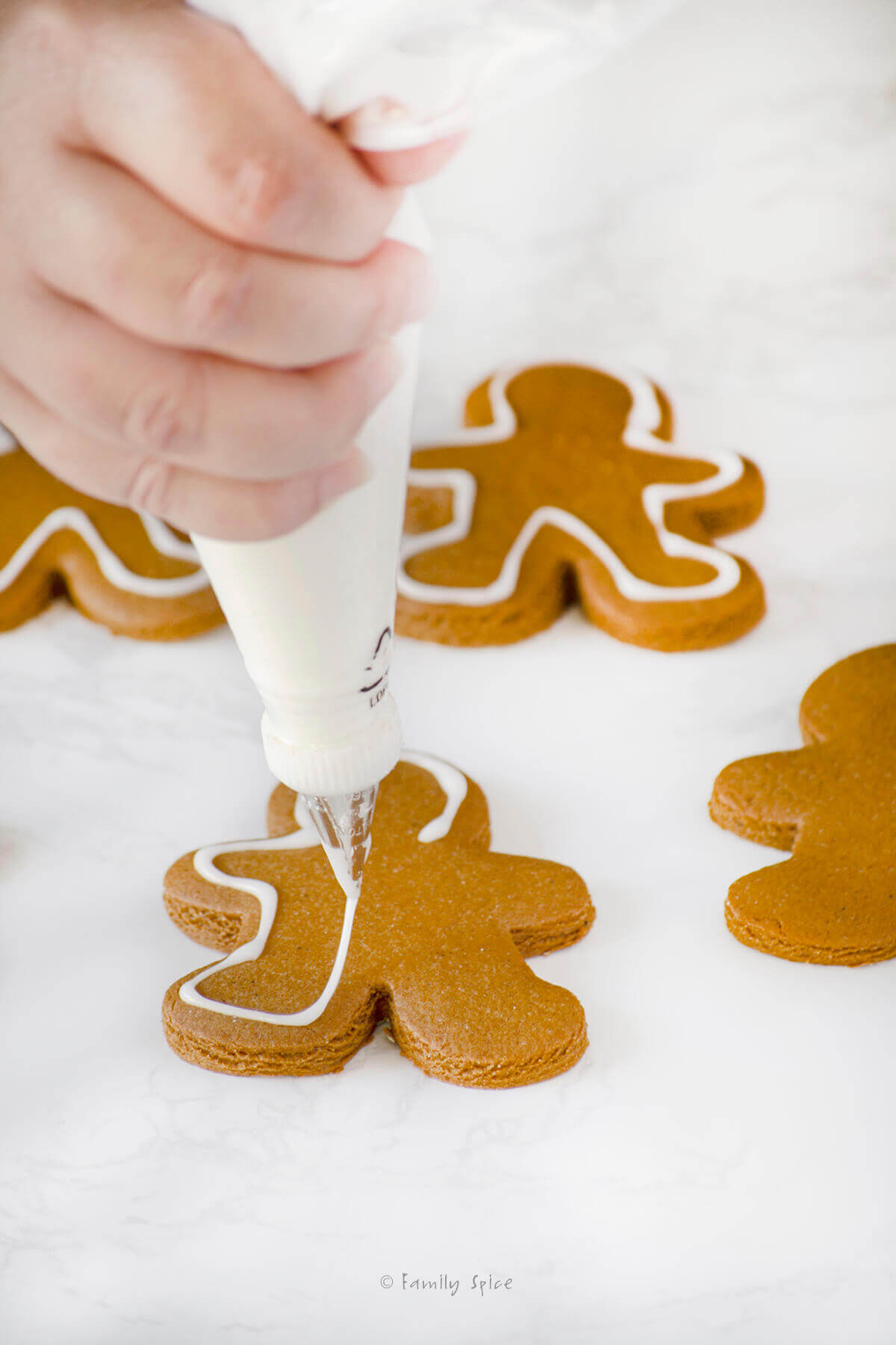 Icing a white border around the edges of a gingerbread man cookie