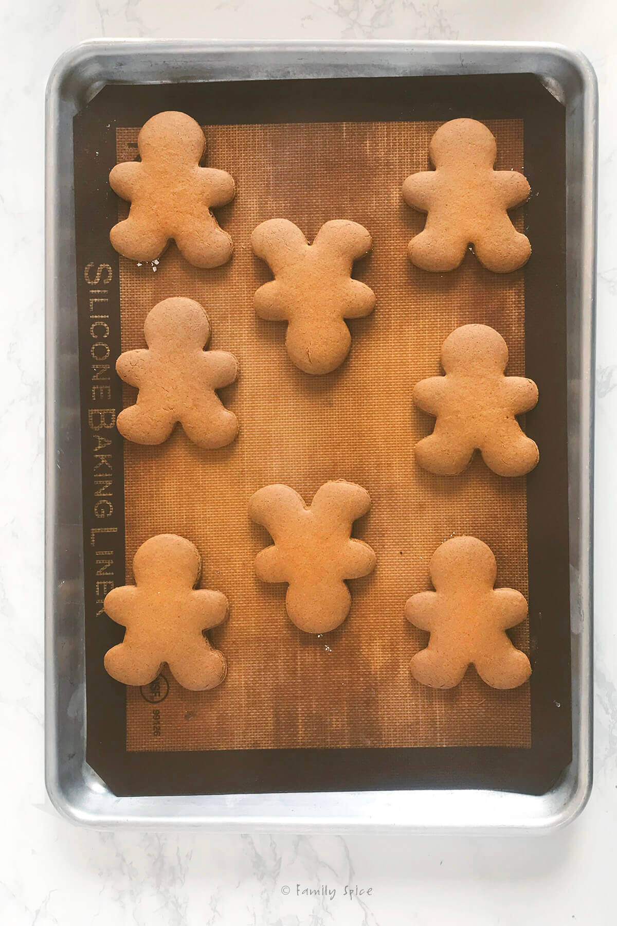 Freshly baked gingerbread men cookies on a baking sheet lined with silicone baking mat