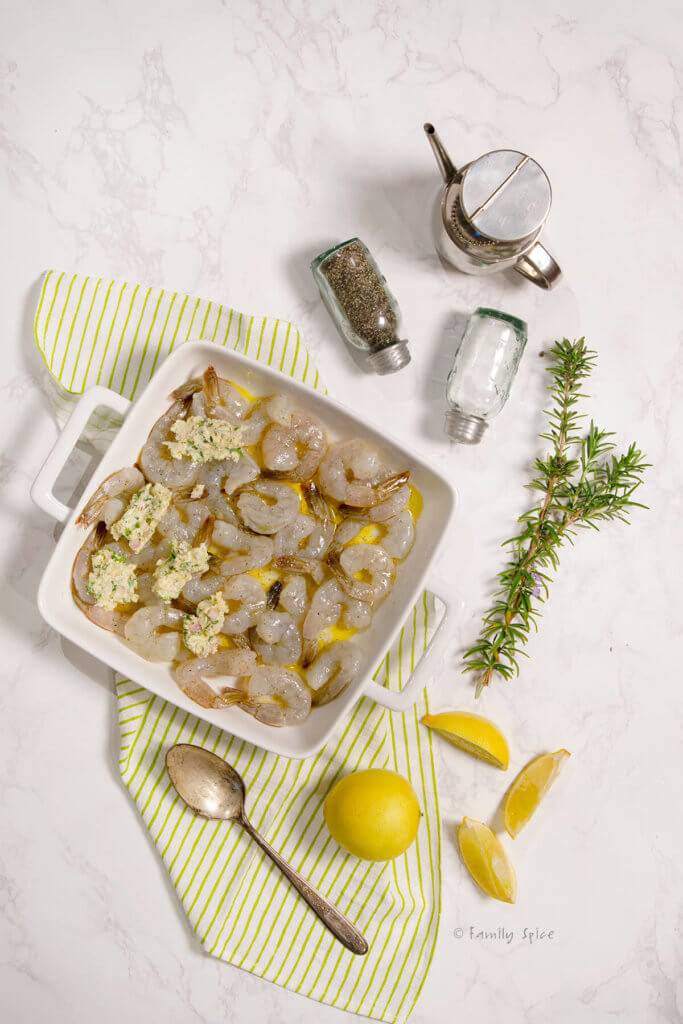 Assembling baked shrimp scampi in a square baking dish with ingredients around it
