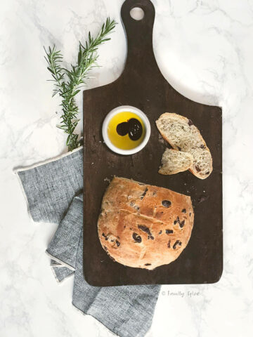 kalamata olive bread on a cutting board with a small bowl of olive oil and balsamic vinegar