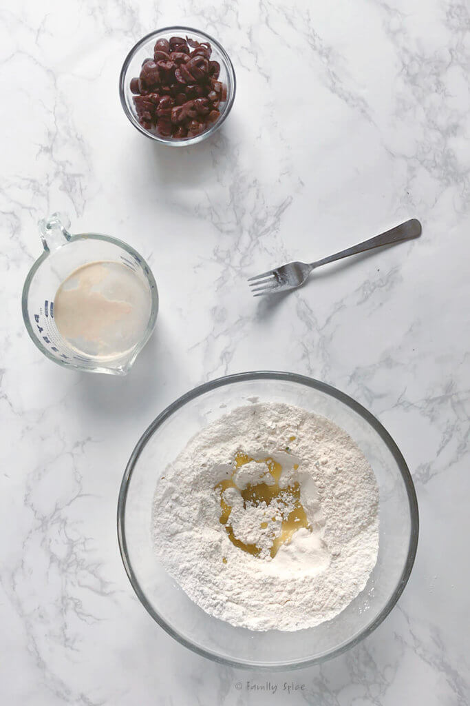 Adding olive oil to a bowl of flour to make bread