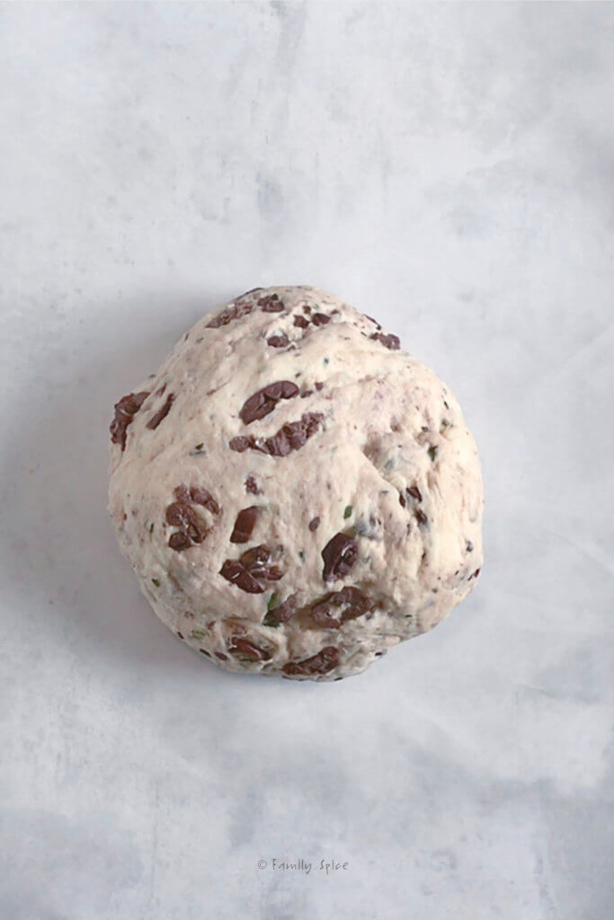Kalamata olive bread dough in a ball on a parchment paper lined baking sheet