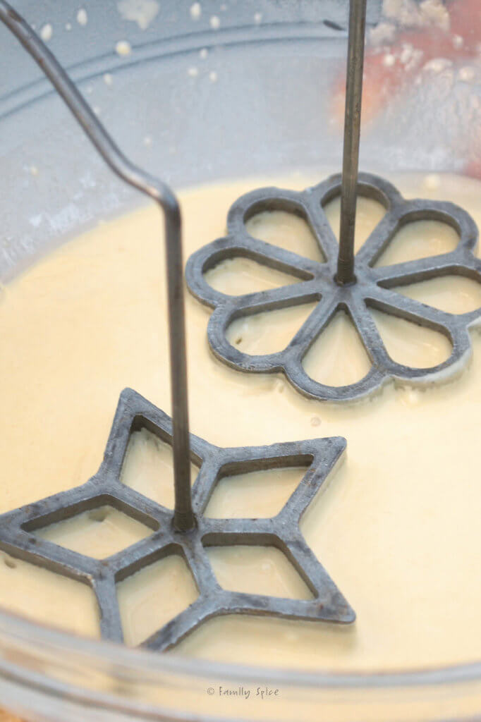 Placing a star and a flower shaped rosette iron in the rosette batter