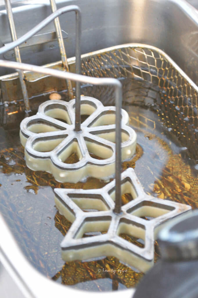 Placing a star and a flower shaped rosette iron coated in batter into hot oil